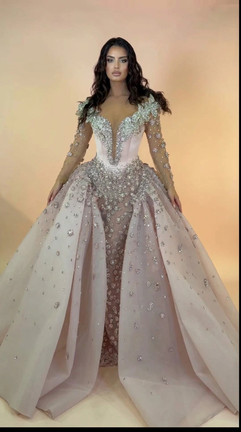 Front view of blush pink crystal beaded ball gown with sheer sleeves and overskirt