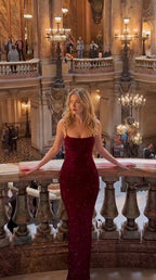 Front view of model wearing a sparkling burgundy spaghetti strap floor-length evening gown on a classical balcony