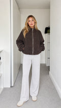 Front full-body view of model wearing dark brown fleece zip-up jacket with white sweatpants