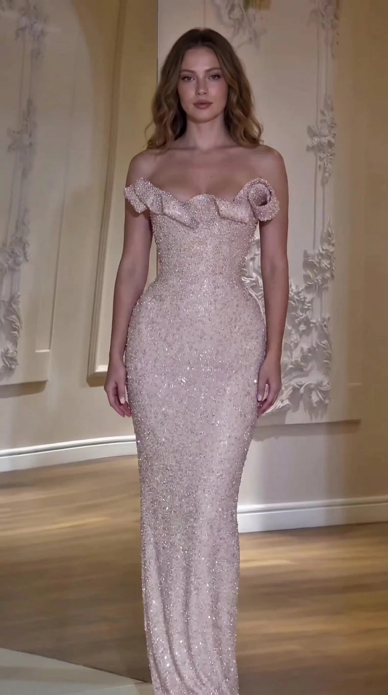 Front view of model wearing a blush pink off-the-shoulder beaded evening gown with rosette neckline