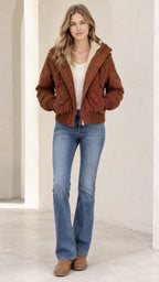 Front view of woman wearing a brown fleece-lined hooded bomber jacket with blue flared jeans