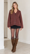 Model wearing a relaxed brown V-neck knit cardigan with button front, black skirt, and knee-high boots