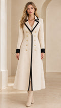 Front full-length view of woman wearing cream maxi coat with black contrast trim and gold crest buttons