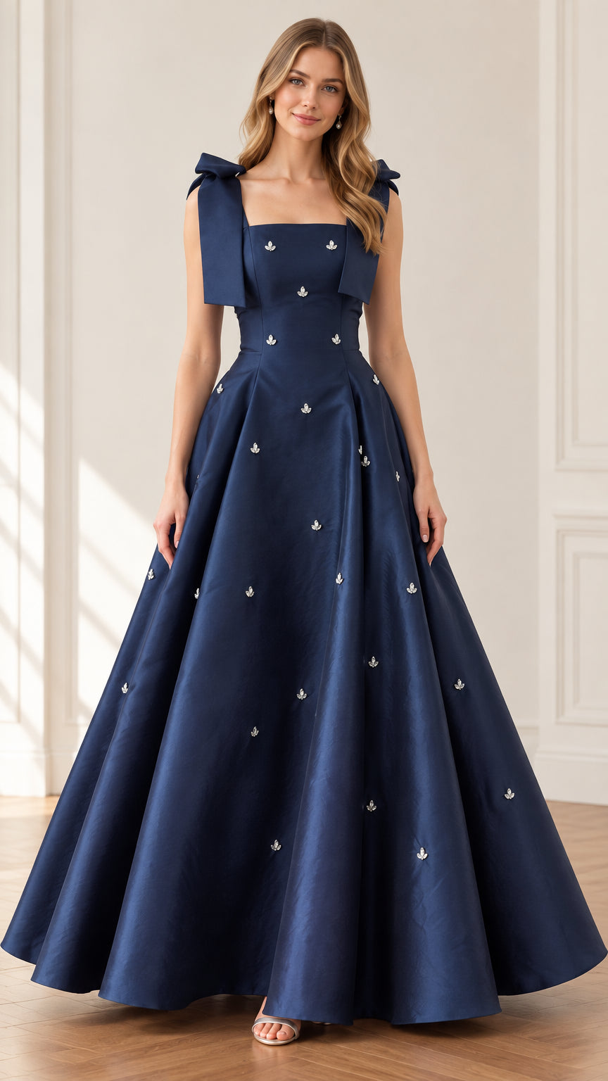 Front full view of woman wearing navy blue bow shoulder crystal embellished A-line evening ball gown