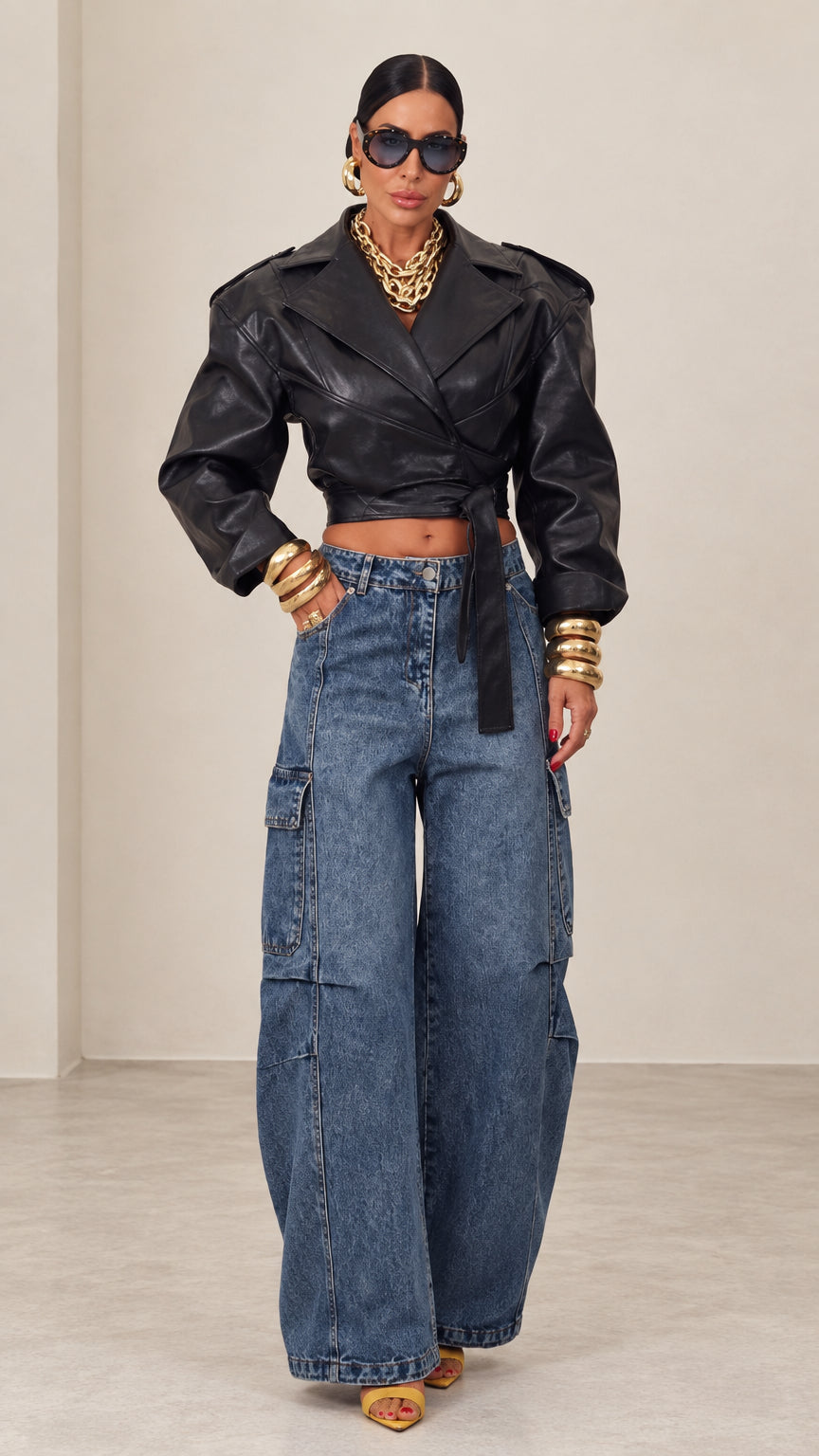 Model wearing black cropped faux leather wrap jacket with wide-leg blue denim jeans, front view