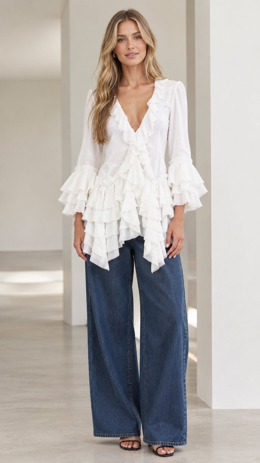 Front view of model wearing white tiered ruffle blouse with wide-leg jeans