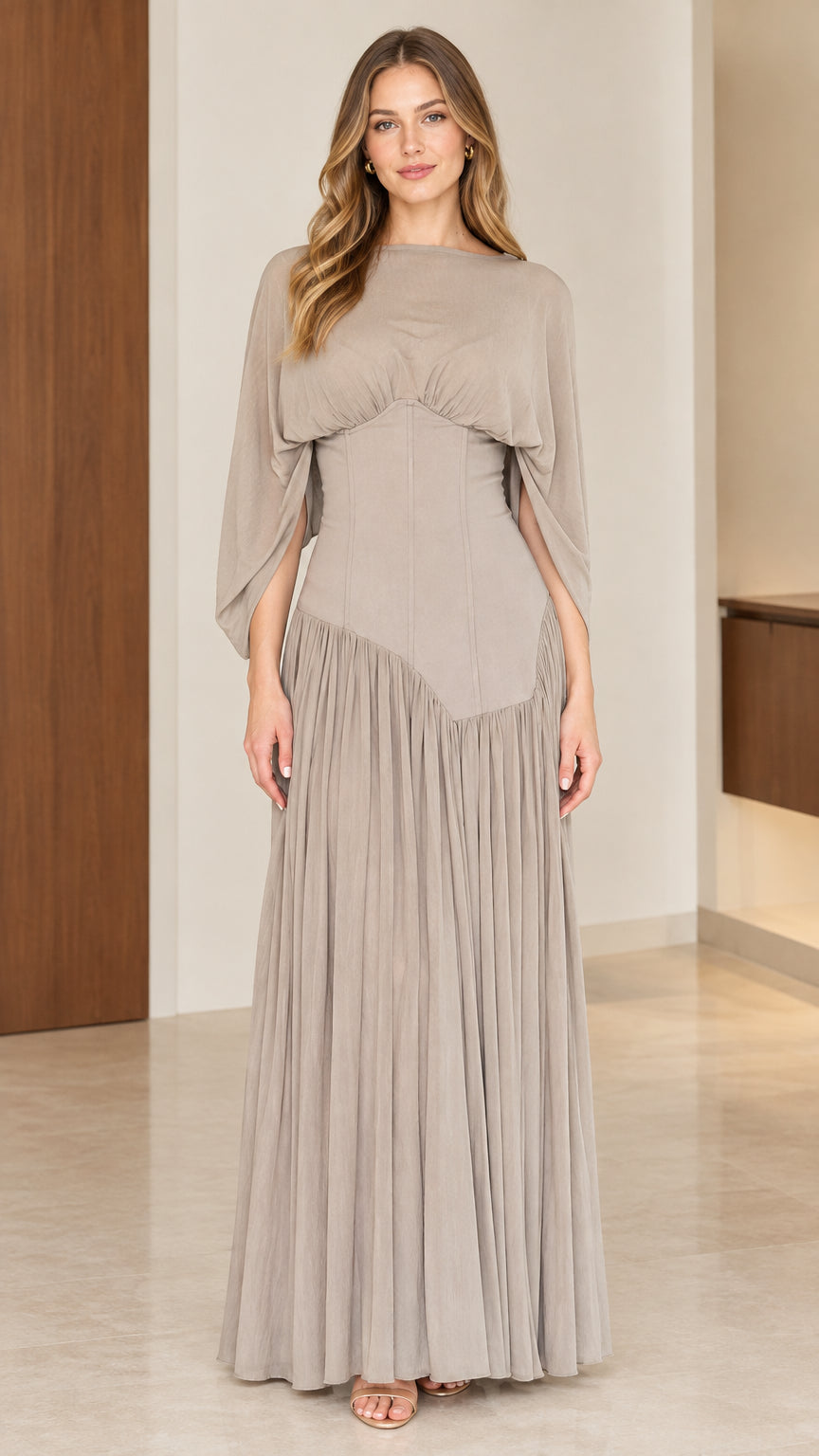 Front full-length view of woman wearing taupe pleated maxi dress with split capelet sleeves