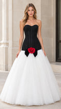 Front view of woman wearing strapless black corset ball gown with white tulle skirt and red rose detail