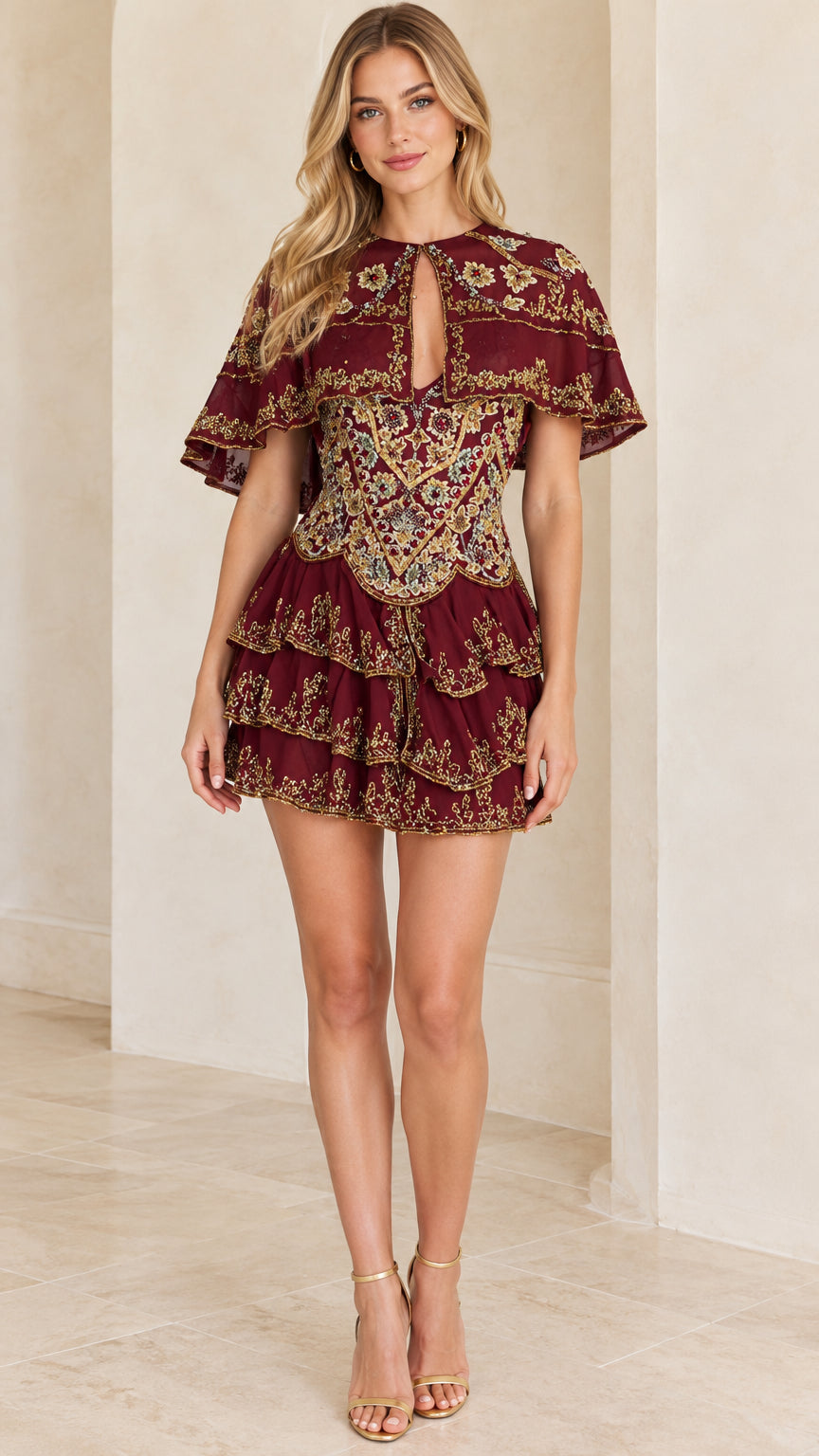 Front view of woman wearing a burgundy embroidered capelet tiered mini dress