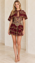 Front view of woman wearing a burgundy embroidered capelet tiered mini dress