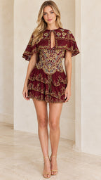 Front view of woman wearing a burgundy embroidered capelet tiered mini dress