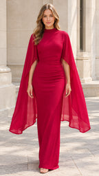 Front view of woman wearing a red mock neck cape maxi dress with ruched waist