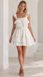 Front view of model wearing white ruffle lace tiered mini dress with strappy heels