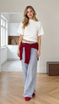 Front full view of woman wearing white short-sleeve knit top, blue striped wide-leg pants, and burgundy waist-tied knit