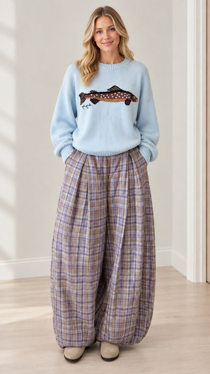 Full front view of model wearing light blue fish graphic sweater and purple-toned plaid balloon pants set