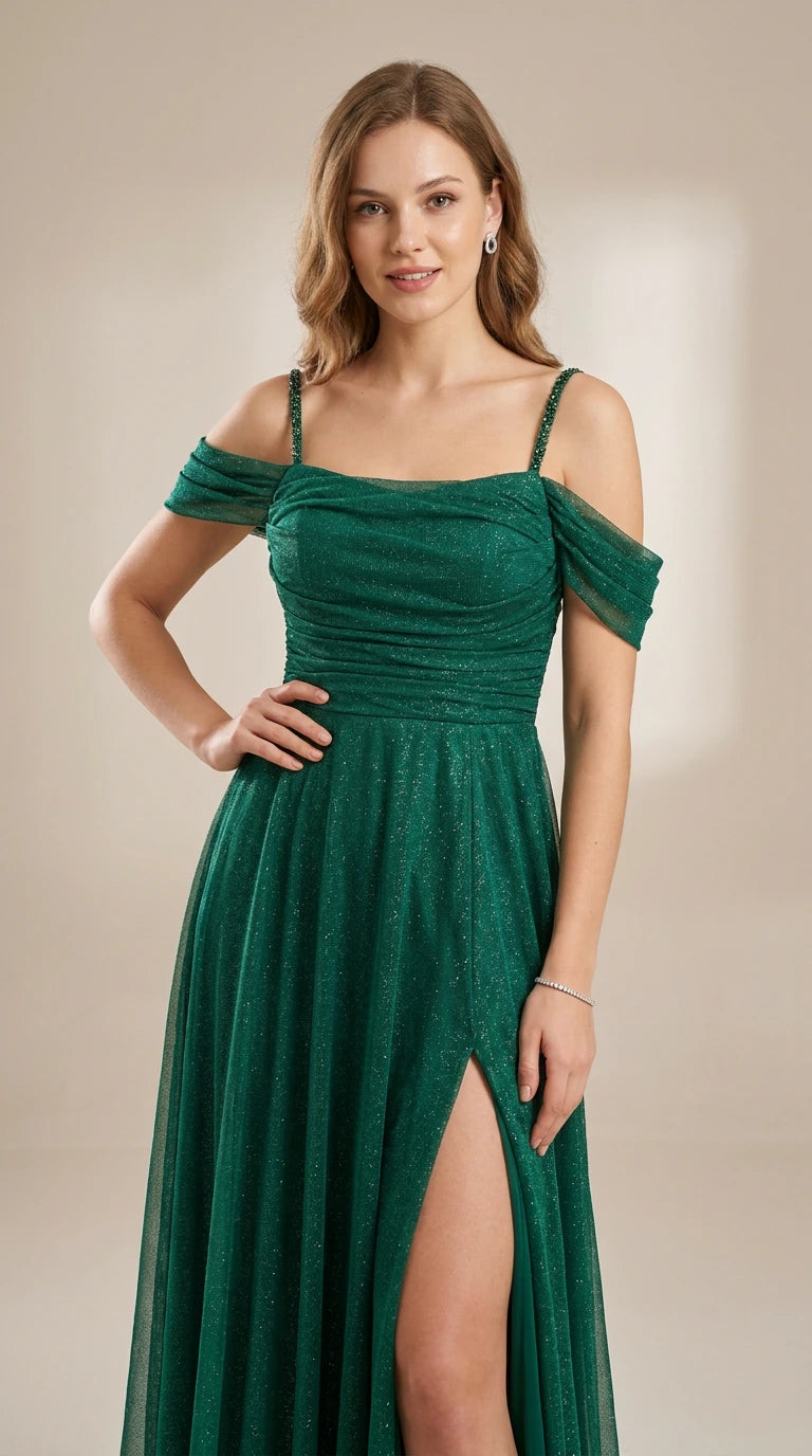 Model wearing an emerald green glitter off-the-shoulder evening gown with beaded straps and thigh slit, front view