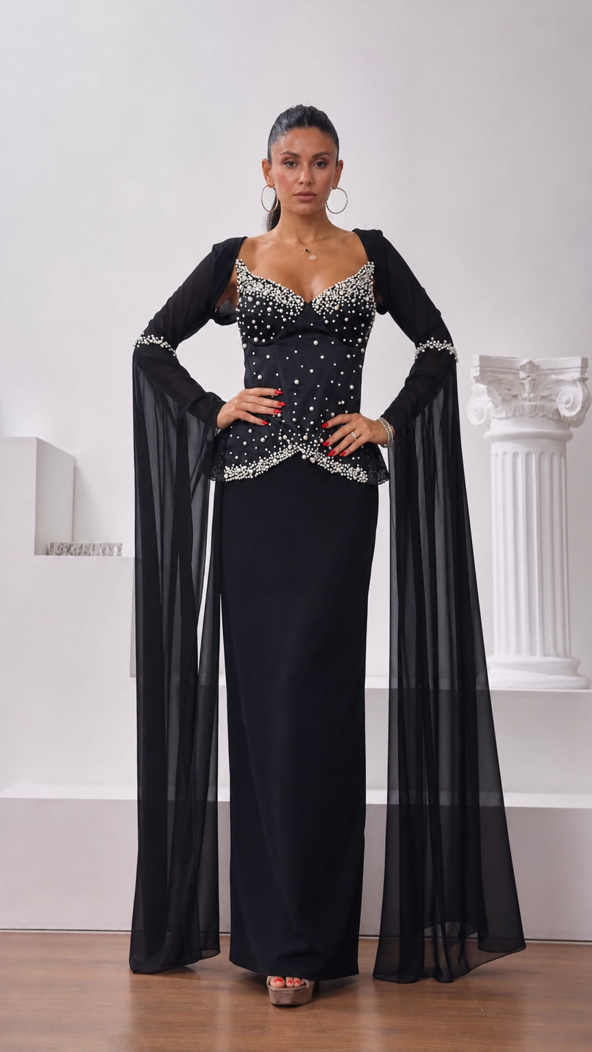 Front view of model wearing black pearl-embellished corset maxi dress with long chiffon cape sleeves