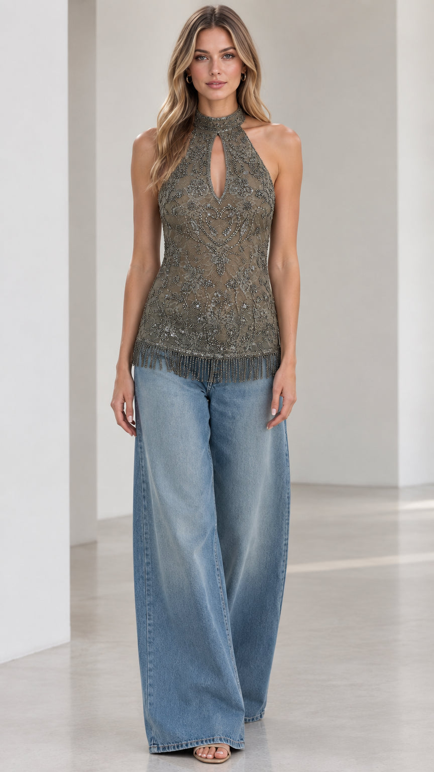 Model wearing an olive embellished halter top with keyhole cutout and beaded fringe paired with wide-leg jeans, front full view