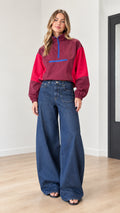 Front view of woman wearing burgundy and red color-block half-zip windbreaker with wide-leg jeans
