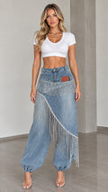 Front full view of light blue denim pants with asymmetrical skirt overlay and sparkling rhinestone fringe