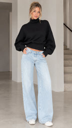 Front view of model wearing black high neck lantern sleeve sweater with light wash wide leg jeans