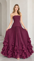 Front view of model wearing strapless burgundy corset ball gown with pleated skirt and 3D floral hem