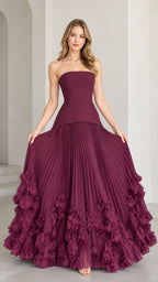 Front view of model wearing strapless burgundy corset ball gown with pleated skirt and 3D floral hem