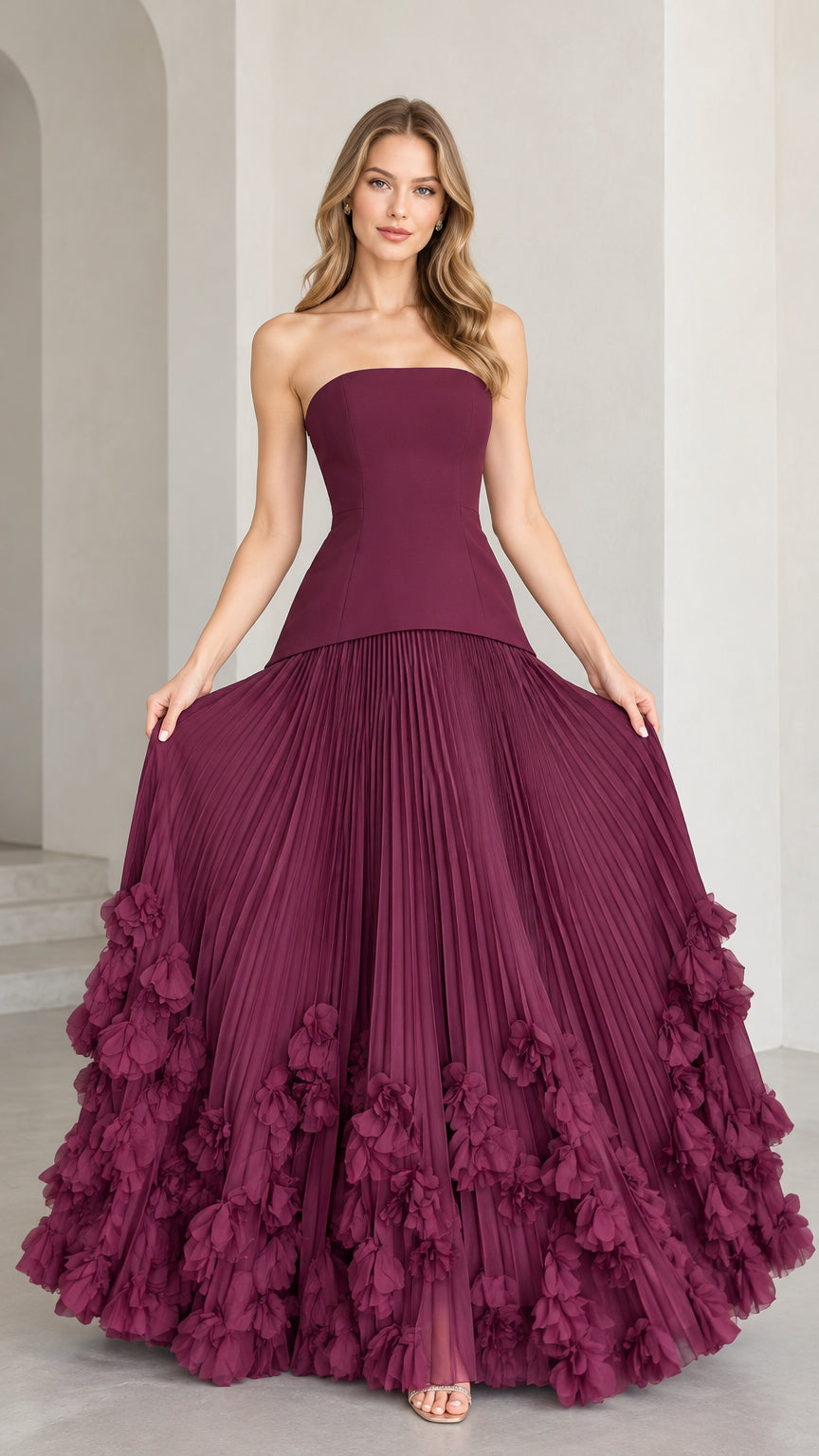 Front view of model wearing strapless burgundy corset ball gown with pleated skirt and 3D floral hem