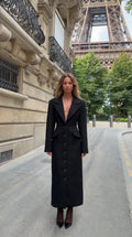 Front view of model wearing black tailored notch lapel maxi coat in Paris