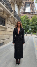 Front view of model wearing black tailored notch lapel maxi coat in Paris