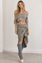 Front full view of woman wearing sage green off-shoulder crop top, draped midi skirt, and leg warmers