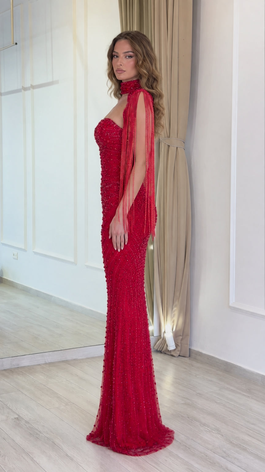 Side profile view of red beaded formal gown with flowing fringe sleeve details