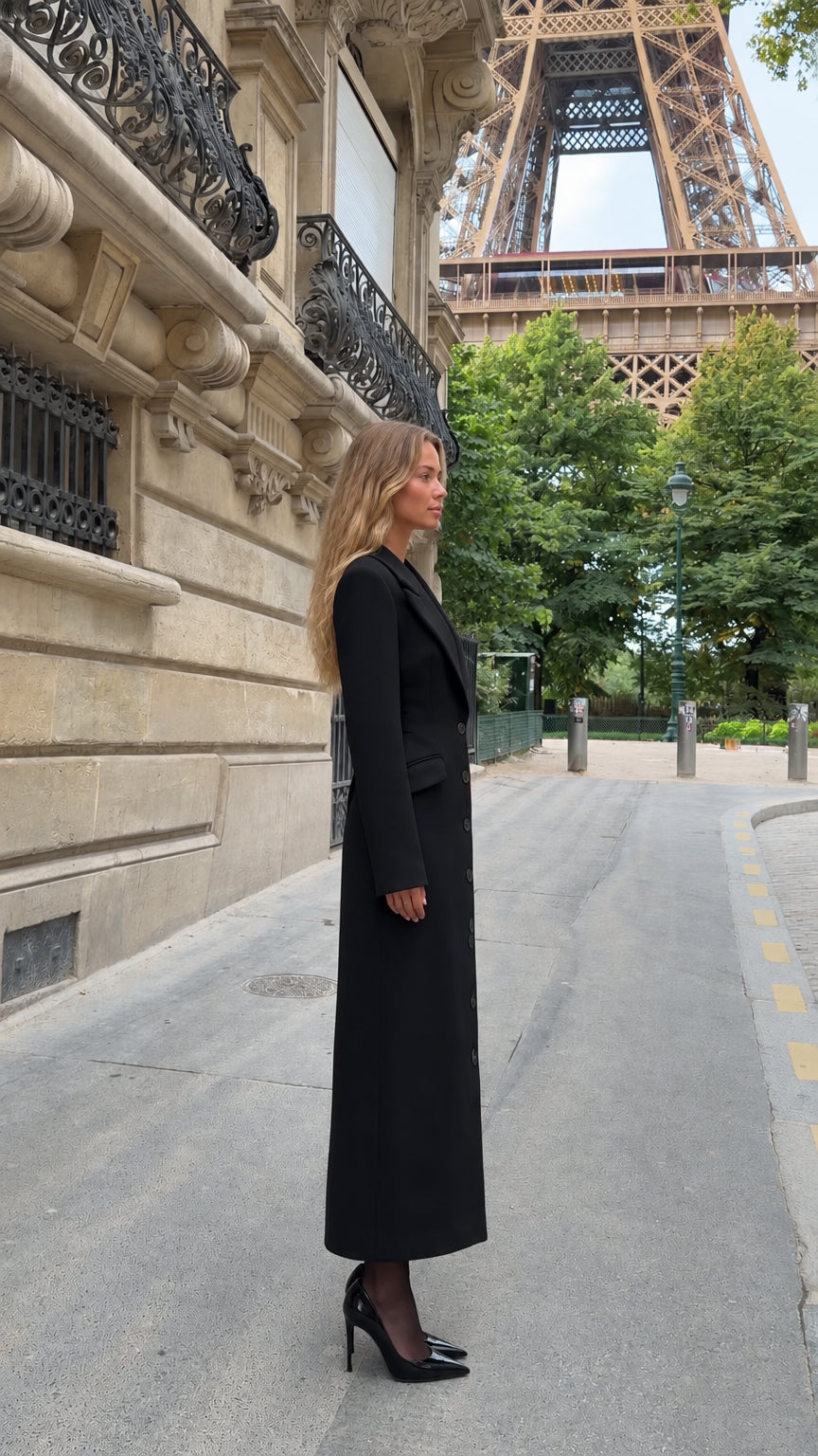 Side profile view of model wearing black structured ankle length coat