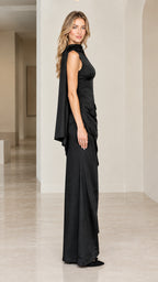 Side profile view of black sleeveless evening maxi dress showing waist draping and shoulder cape detail
