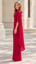 Side profile of woman wearing a red maxi gown with sheer cascading cape sleeve overlay