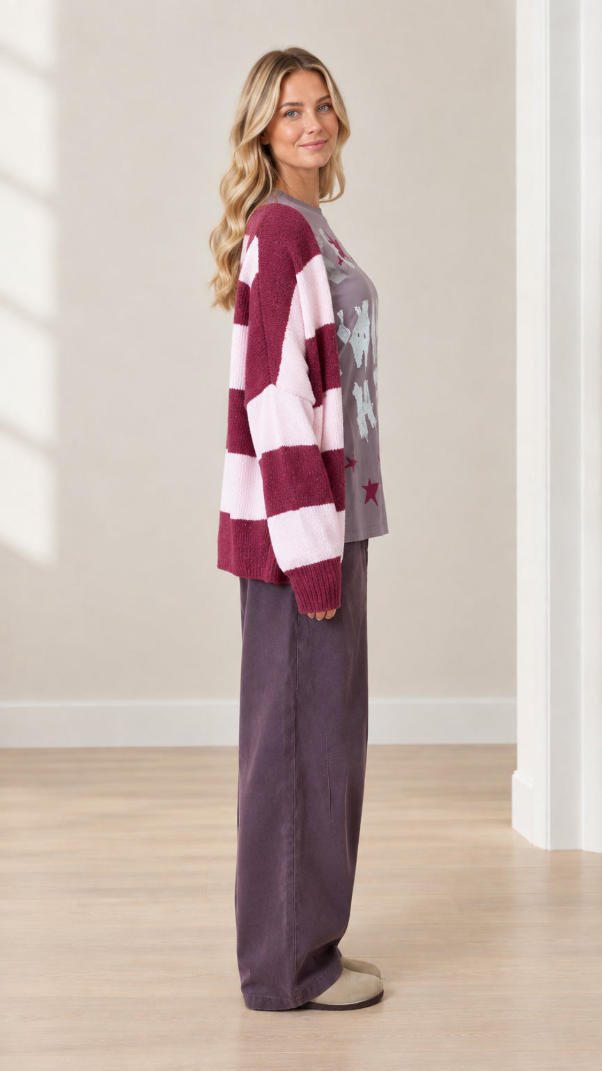 Side view of model wearing purple graphic top, wide-leg trousers, and striped knit cardigan