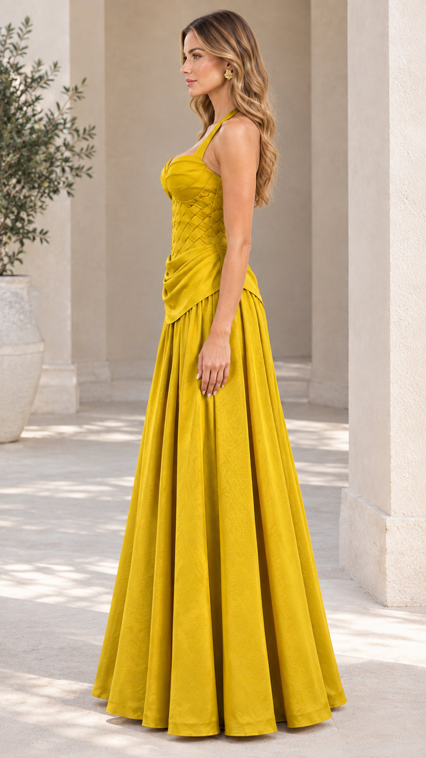 Side profile of model wearing yellow halter maxi formal gown in an architectural setting