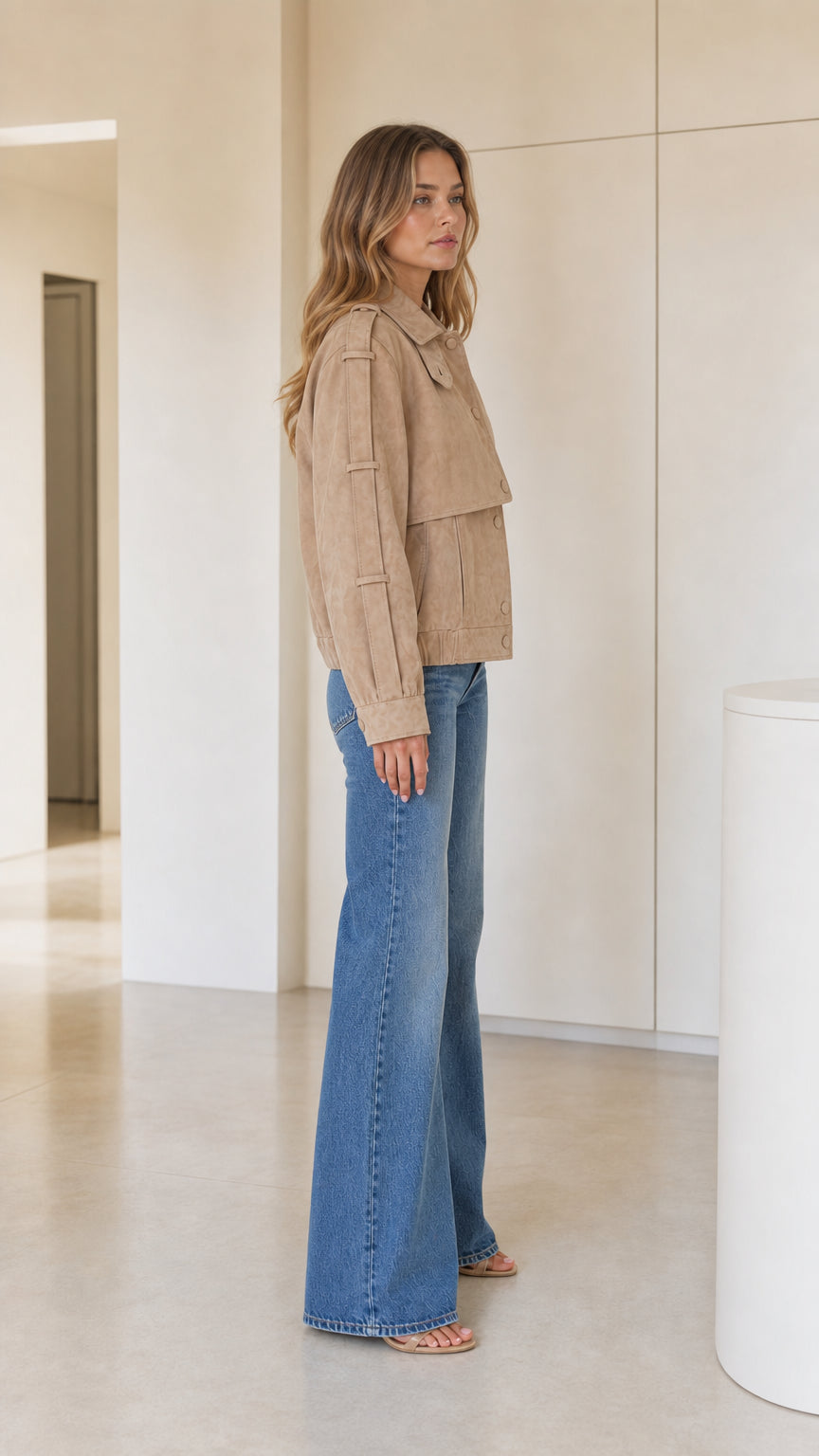 Side profile view of model wearing camel faux suede jacket and denim trousers