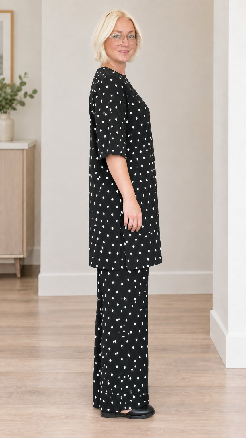 Side profile view of woman wearing black polka dot tunic and matching trousers