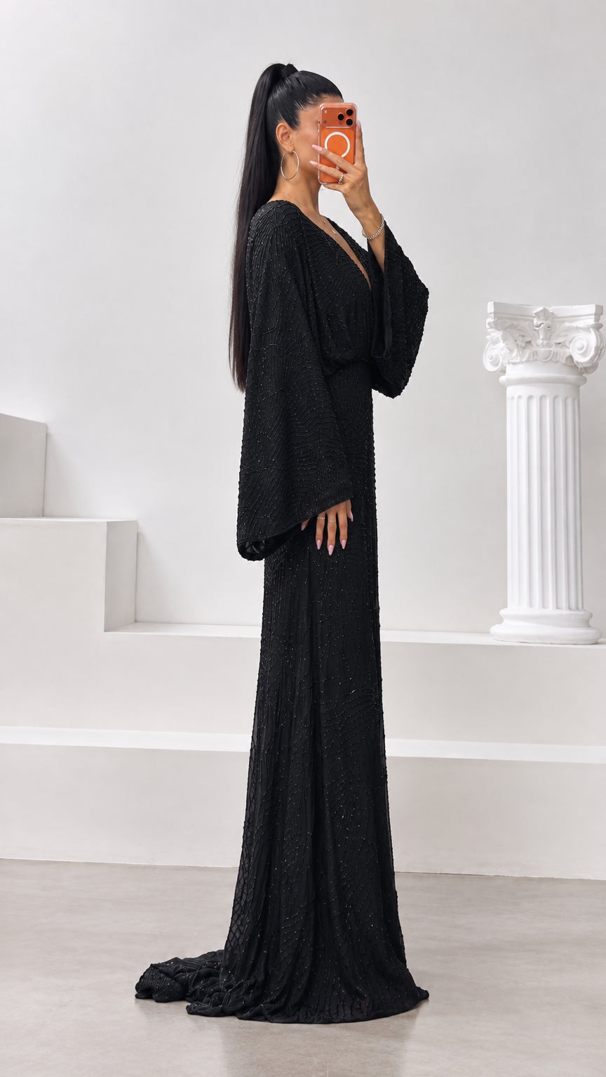 Side profile of black long sleeve beaded maxi gown showing floor-length drape