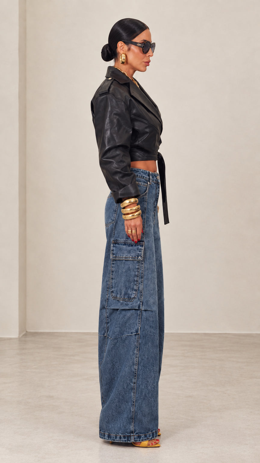 Side view of black cropped faux leather wrap jacket paired with wide-leg denim jeans