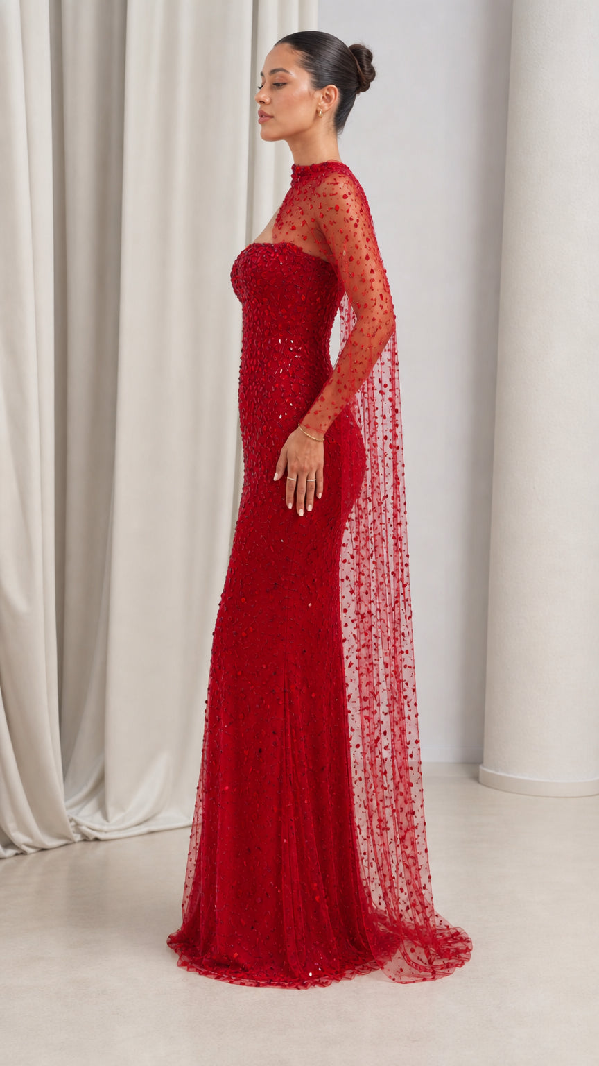 Side profile view of red embellished mermaid formal gown showing draped cape sleeve