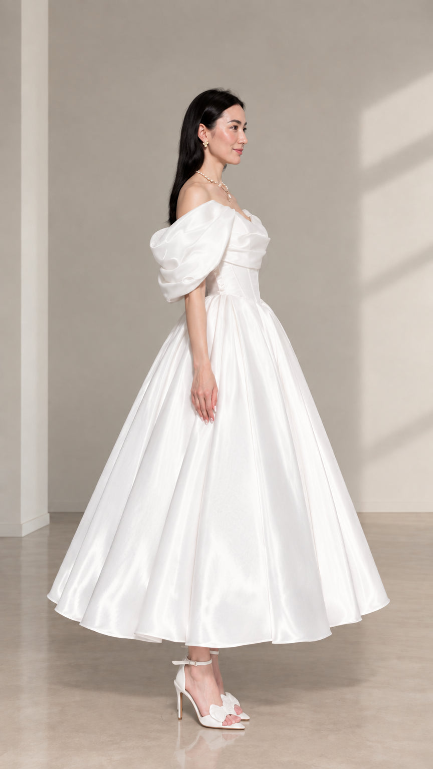 Side-angle view of white off-the-shoulder satin midi evening dress with pleated skirt
