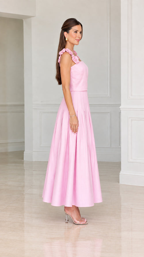 Side profile view of woman modeling pink pleated midi dress with floral shoulder accents