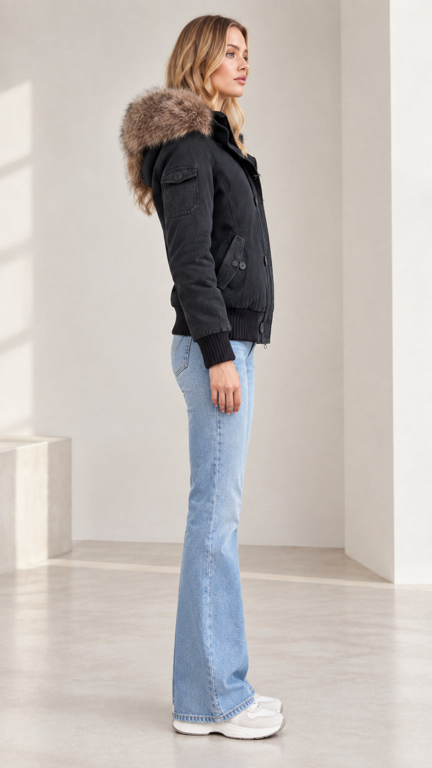 Side profile view of model wearing black fleece-lined bomber jacket with faux fur hood