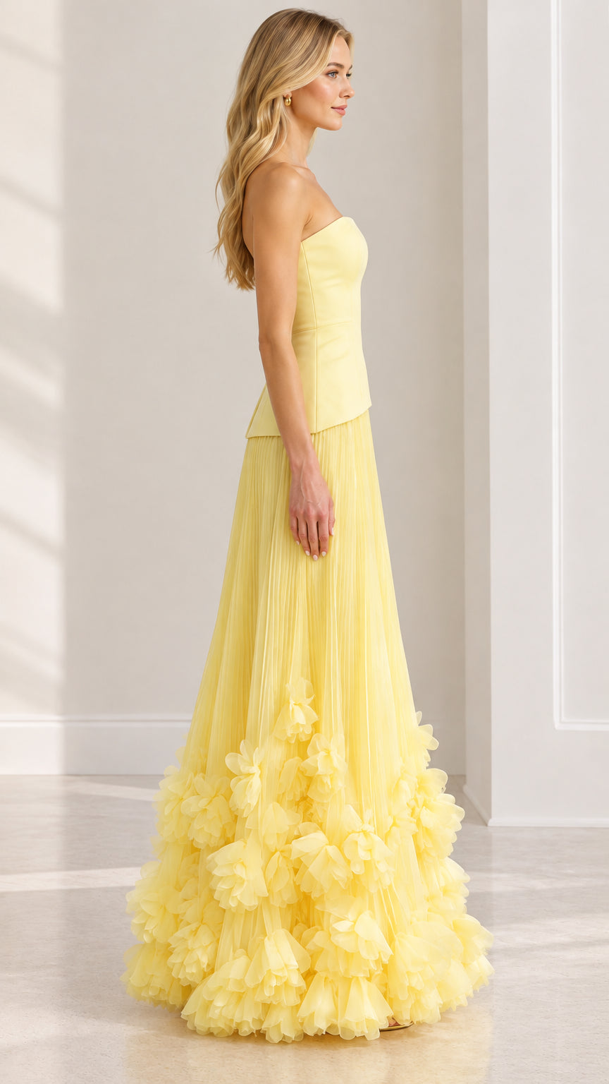 Side profile of strapless pastel yellow evening gown showing flowing pleated silhouette