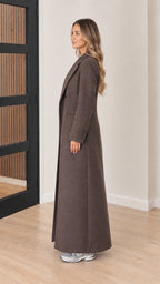 Side profile view of model showcasing the long silhouette and drape of the brown maxi coat