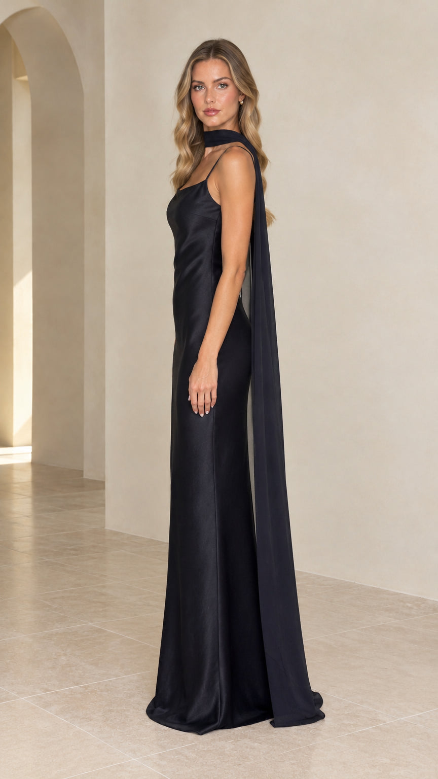 Side profile view of black satin maxi dress showing the flowing cape detail