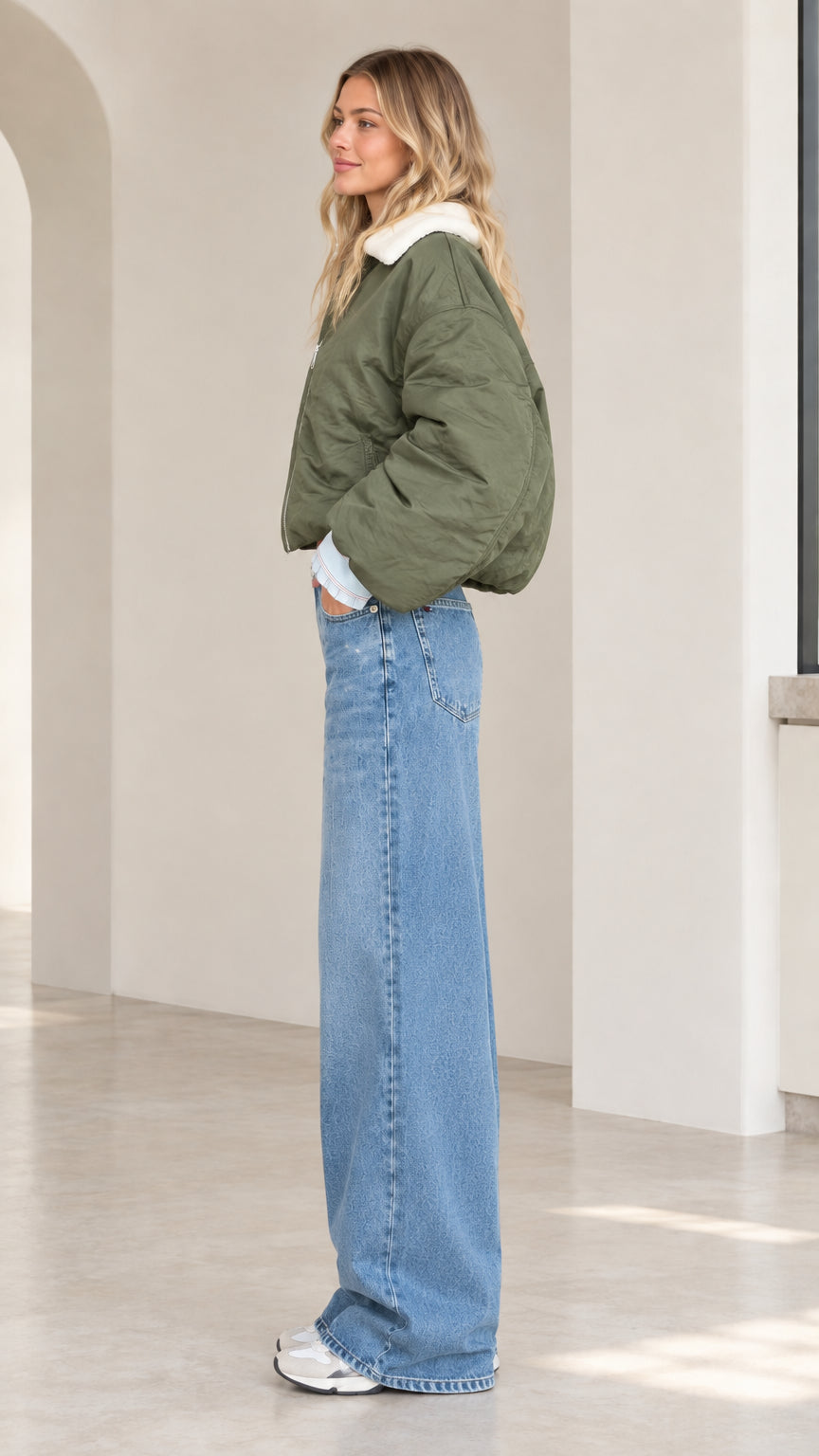 Side profile view of model wearing olive green cropped bomber jacket with wide leg denim
