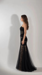 Side profile view of woman modeling black strapless ruched lace mermaid formal dress